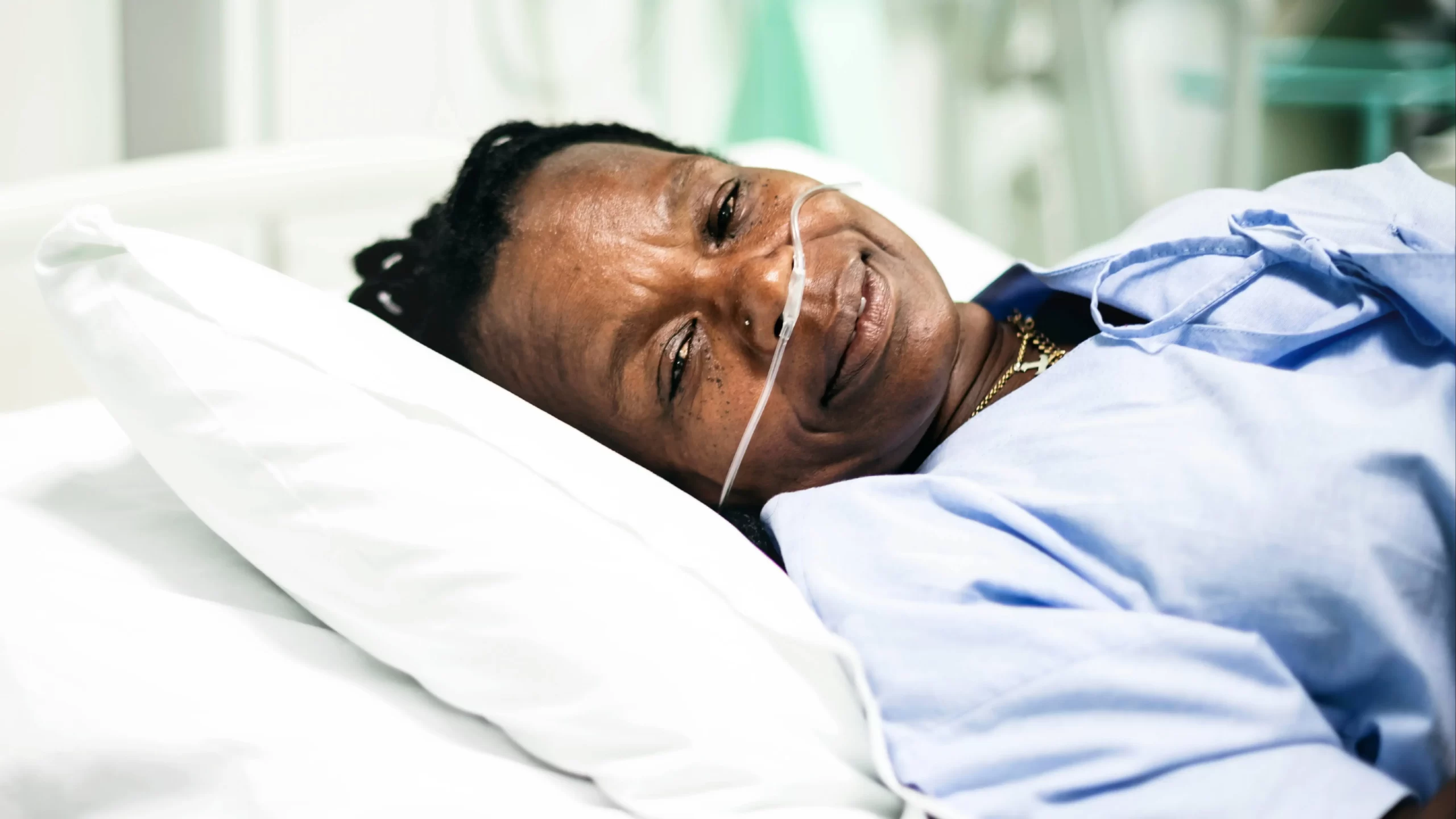 an African American woman slightly smiling in a hospital gown resting on a pillow with oxygen tubes in her nose 16x9 1 scaled